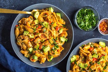 Gray plate filled with shell pasta with diced chicken, avocado pieces, and diced tomatoes in a creamy sauce