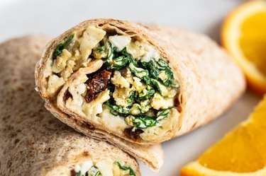close up of the inside of a breakfast burrito with eggs, mushrooms, tomatoes and hummus