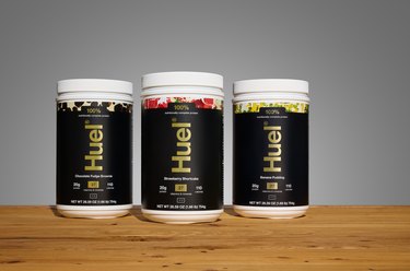 three containers of Huel flavored protein powder on a table