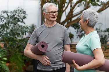 an over 60 couple holding purple yoga mats under their arms