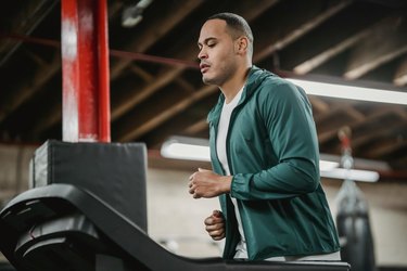 an adult wearing a green zip-up hoodie jogs on a treadmill