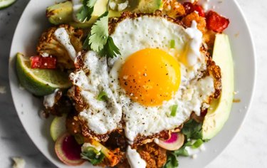 Skillet Chipotle-Cauliflower Chilaquiles with a fried egg and lime wedges on a white plate