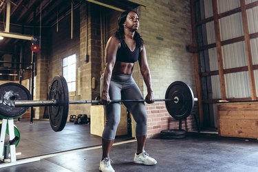 woman deadlifting barbell in industrial-looking gym