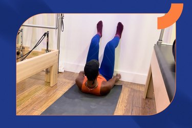 Pilates instructor in blue leggings and an orange top does a wall pilates workout for beginners