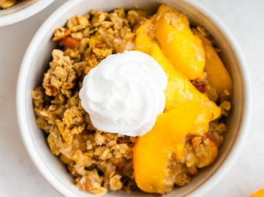 Healthy Peach Crisp in a white bowl with whipped cream topping