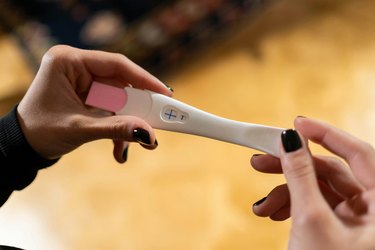 a close up of an adult's hands with black nail polish holding a pregnancy test trying to determine if they have a pregnant belly or belly faat