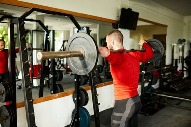 Fit amputee wearing a red shirt does a barbell squat variation at the gym