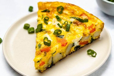 Potato and spinach frittata on a white plate with chives on top