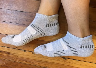 two feet against a wood background wearing the Bering ankle socks in gray