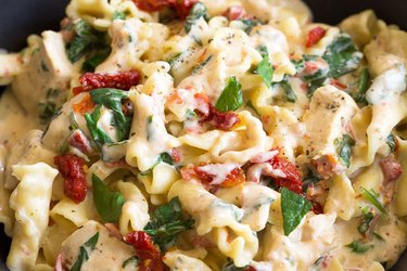 Bowl of penne pasta with diced chicken, spinach and sundried tomatoes in a creamy sauce/