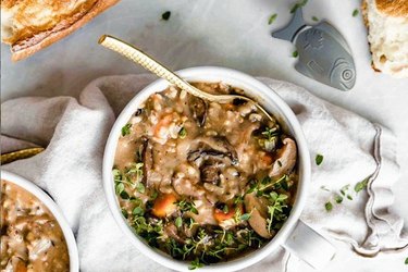 bowl of grains and vegetable soup with iron fish next to it on a white table