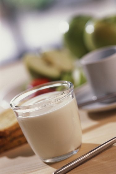 一杯牛奶放在桌子上，旁边有杯子、碟子、餐具和四片面包，特写、倾斜、选择性聚焦