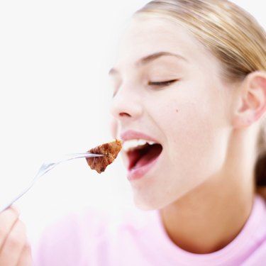 Close-up of a teenage girl (16-18) eating a piece of steak on a fork