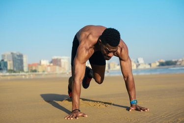 Mountain climbers exercise. Fit man warming up before running at the beach. Black athlete on hiit cardio outdoor workout.