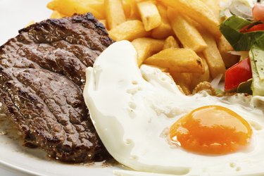 Beefsteak, fried egg, French fries and vegetables