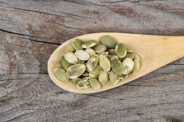Raw pumpkin seeds in a wooden spoon on a wooden table
