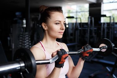 Young beautiful woman doing biceps curl with EZ curl bar in a gym. Athletic girl doing workout in a fitness center