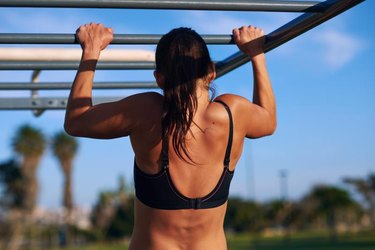 young athletic fitness woman working out at outdoor gym doing pull ups at sunrise