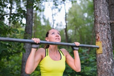 Fit woman training pull ups on horizontal bar in city park outdoors.