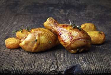 Roasted chicken legs and potatoes on wooden cutting board