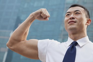 Portrait of young businessman flexing muscle outdoors