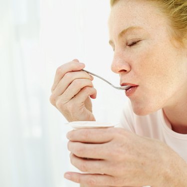 Close-up of a young woman eating strawberry yoghurt with a spoon