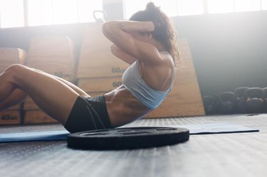 Side view of fit young woman doing pilates, working on abdominal muscles. Fitness woman exercising to improve core muscle strength in gym.