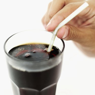 Close-up of a human hand holding a straw in a glass of cola