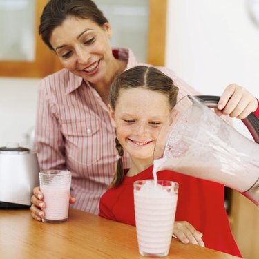 Young mother and a young girl (8-10) pouring out strawberry milk shake from a blender into a glass