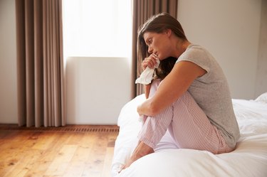 Woman Suffering From Cold Sitting On Bed With Tissue