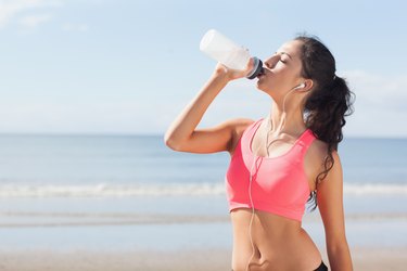 Beautiful healthy woman drinking water on beach