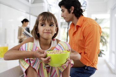 Family at breakfast table, girl (8-10) holding bow of cereal