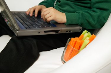 Boy (7-9) using laptop with glass of celery and carrot, low section