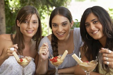 Teenage girl (16-18) and two young women eating dessert, portrait