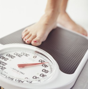 Woman stepping on bathroom scale, low section, Close-up of foot