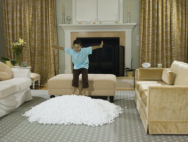 Boy (3-4) jumping into pile of Styrofoam packing peanuts on living room floor