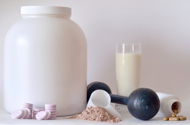 Big jar of protein powder, dumbbell, milk, pills and tablets