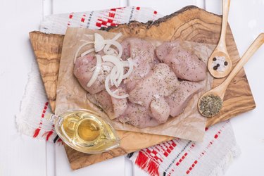 Seasoned raw chicken breast fillets on a wooden board.