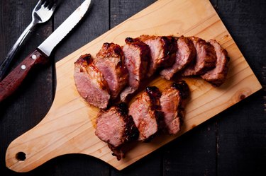 sliced beef and pork roast on cutting board with fork and knife