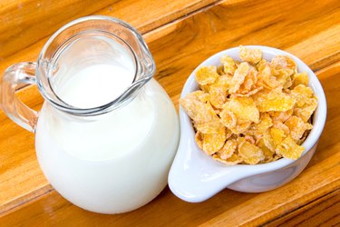 Corn flakes in white bowl and milk on wooden table