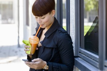 young woman drinking smoothie using mobile phone