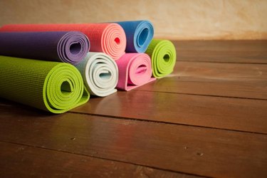 Colorful yoga mats rolled up on a wooden floor in a yoga studio.