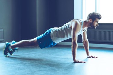 Full length of young handsome man in sportswear doing push-up at gym