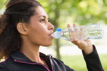 Close up side view of tired woman drinking water in park