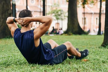 Sportsman doing crunches on grass in park