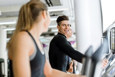 Two adults using ellipticals at the gym.