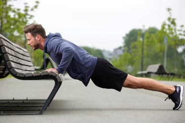 Full length side portrait of attractive man doing pushup outside