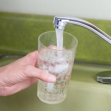 A woman fills a glass of tap water at a kitchen sink.