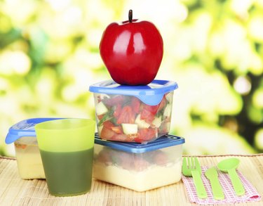 Tasty lunch in plastic containers, on bamboo mat close-up