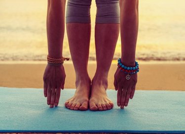 Young woman doing yoga exercise on beach near the sea at sunset in summer, face is not visible